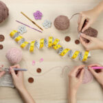 Women crocheting with threads at wooden table, top view